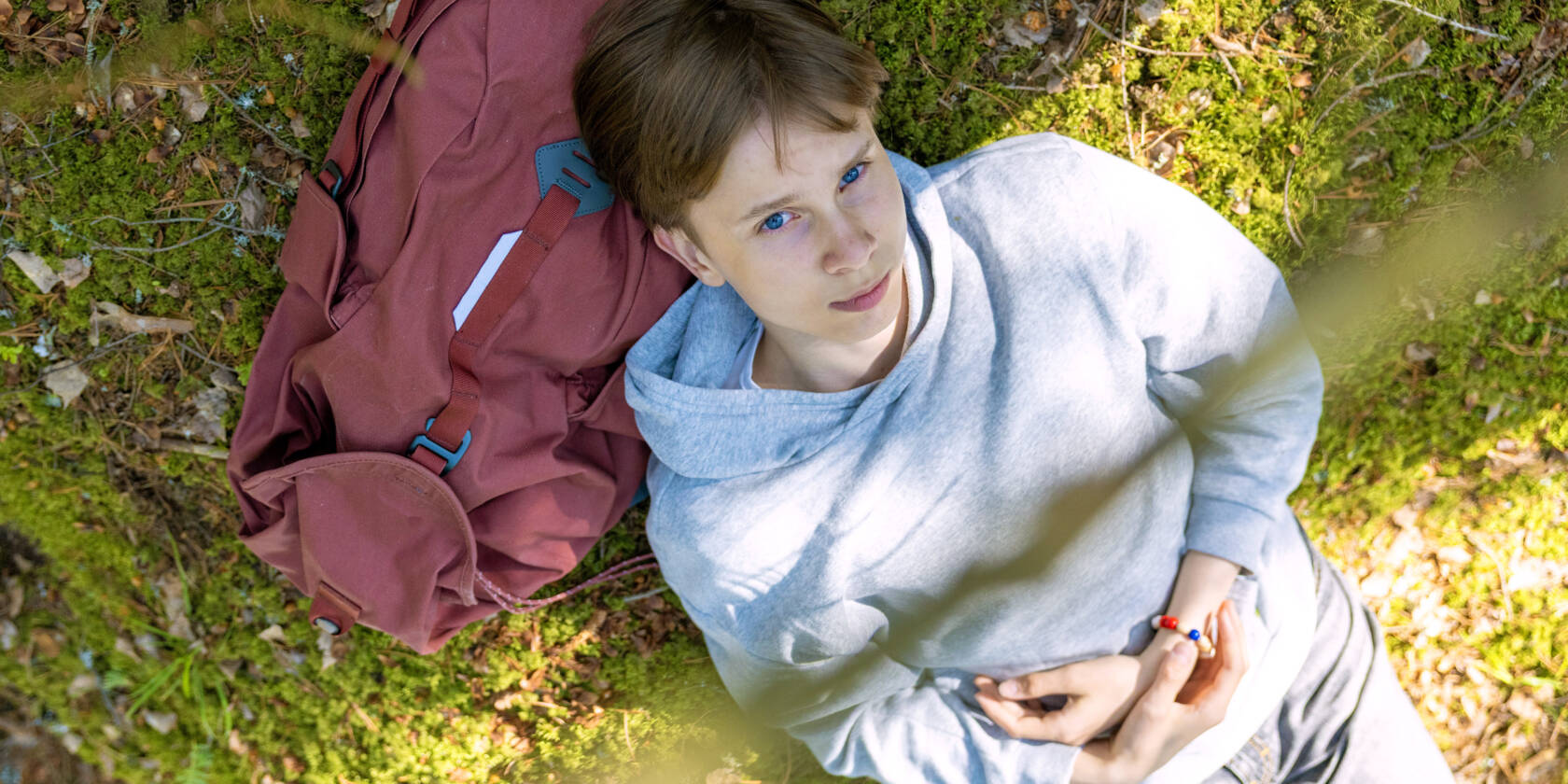Nuori makaa selällään maassa, pää repun päällä.