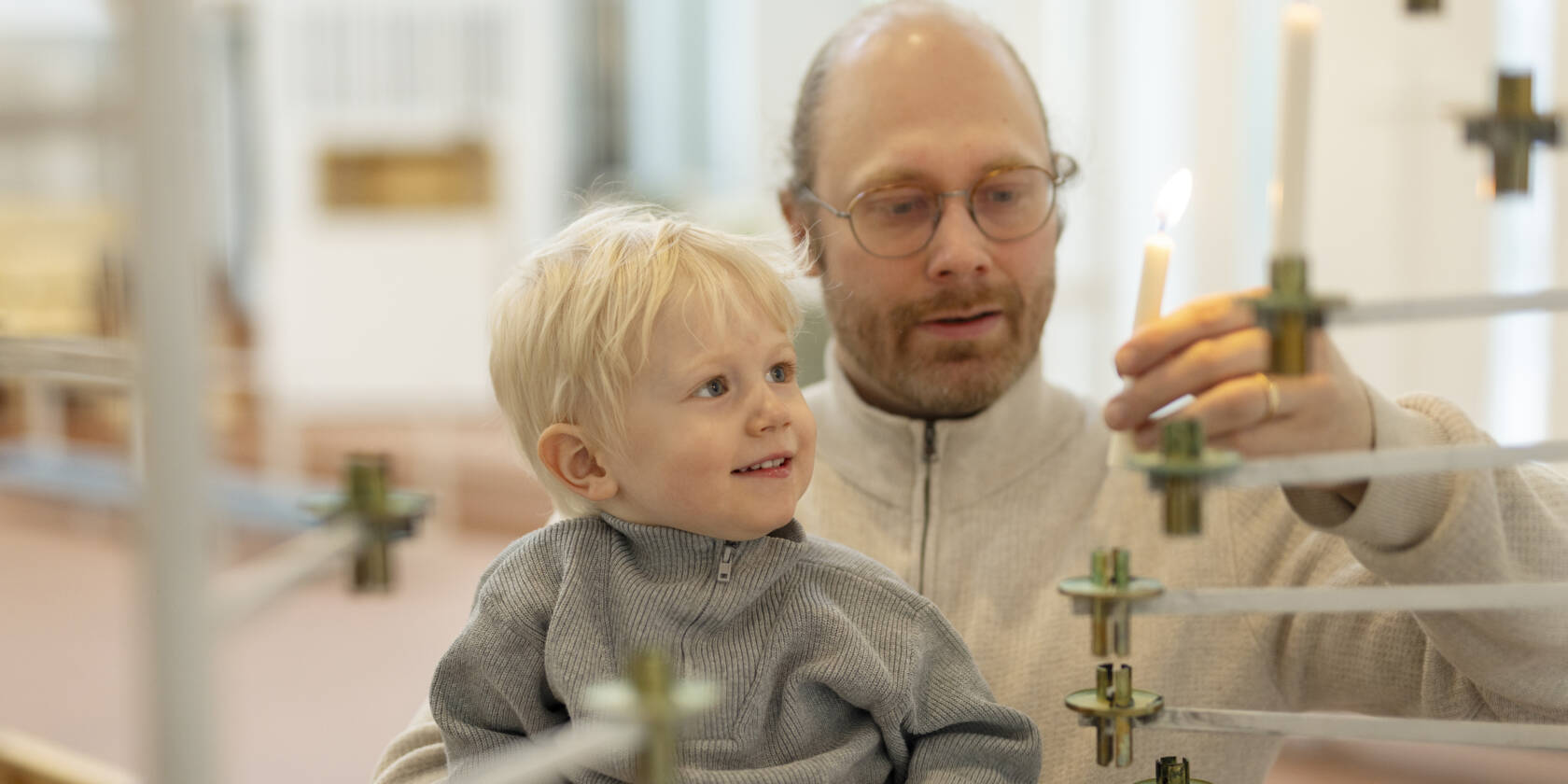 Vanhempi ja lapsi kirkossa sytyttämässä kynttilää lähetyskynttelikköön.