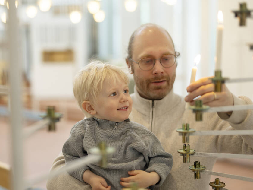 Vanhempi ja lapsi kirkossa sytyttämässä kynttilää lähetyskynttelikköön.