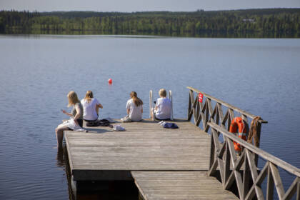 Joukko leiriläisiä istuu laiturin päässä ja uittaa jalkojaan vedessä.