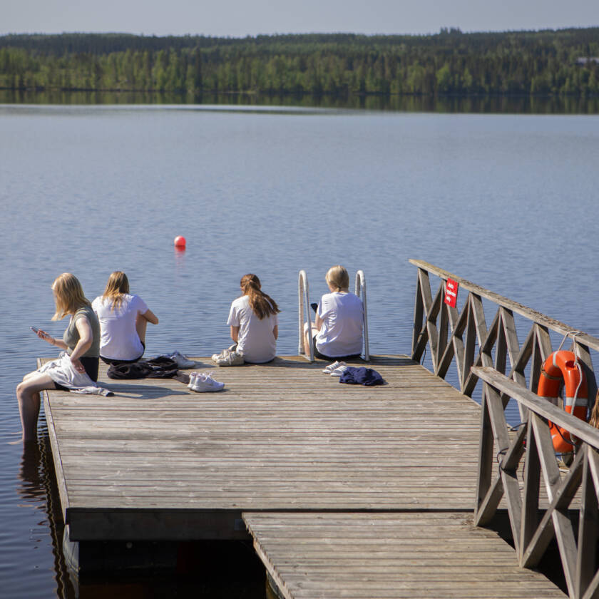 Joukko leiriläisiä istuu laiturin päässä ja uittaa jalkojaan vedessä.
