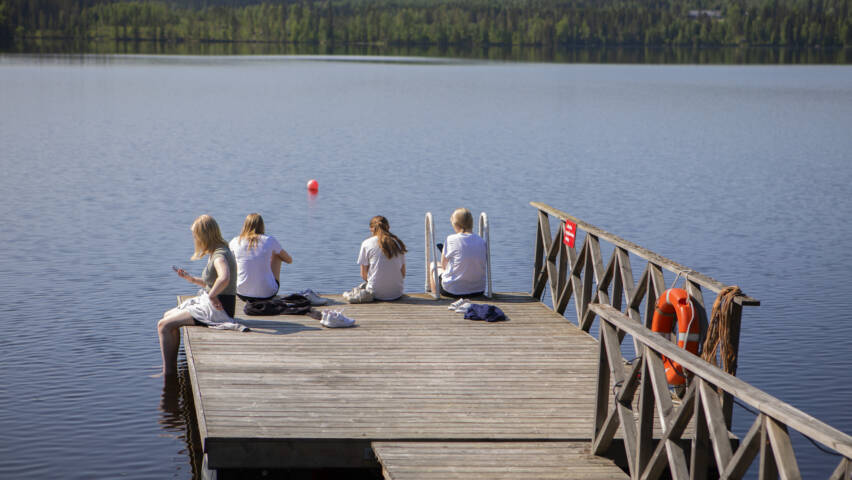 Joukko leiriläisiä istuu laiturin päässä ja uittaa jalkojaan vedessä.