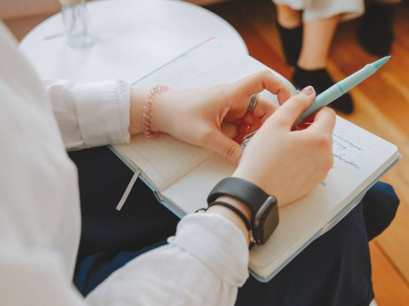 A person is sitting holding a pen and with a notebook in the lap.