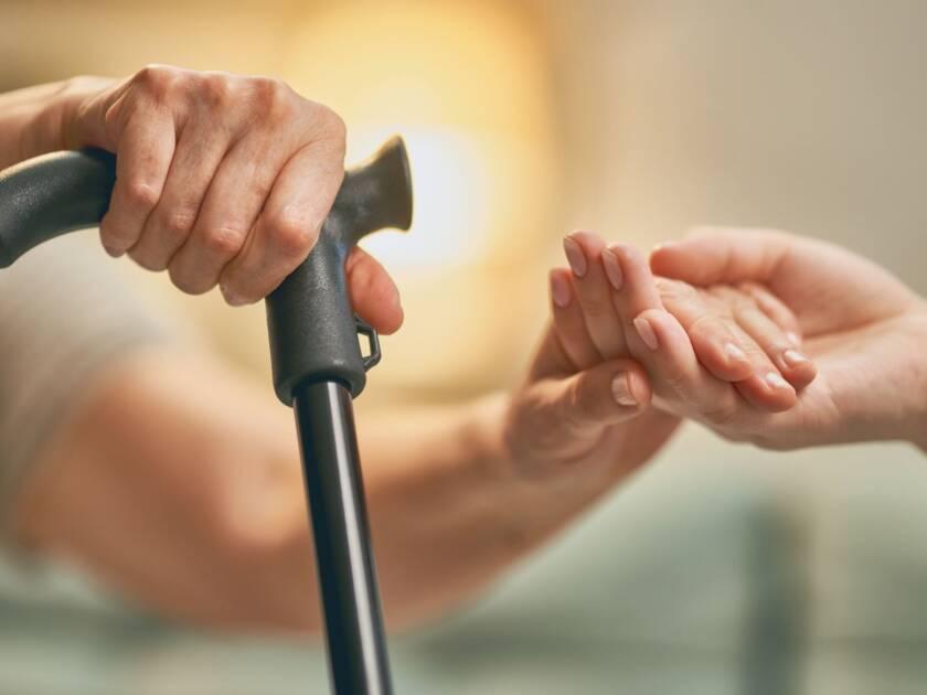 A younger hand is helping an older one with a cane.
