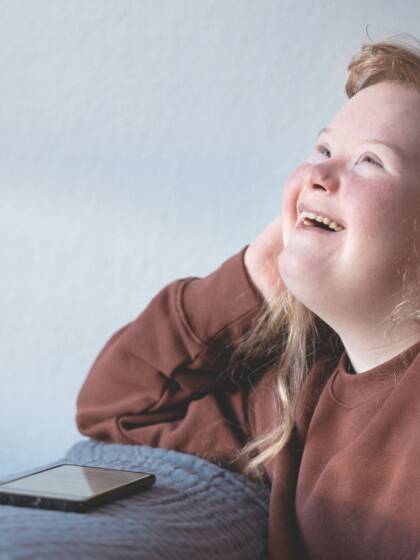A girl is looking up and laughing with a mobile phone in front of her.