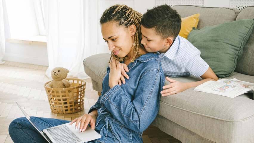 A woman and a child sit by a couch. The child holds his arm around the woman.