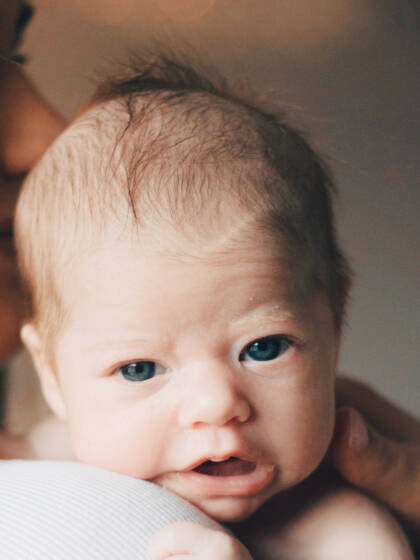 A baby on a woman's shoulder looks straight in to the camera.