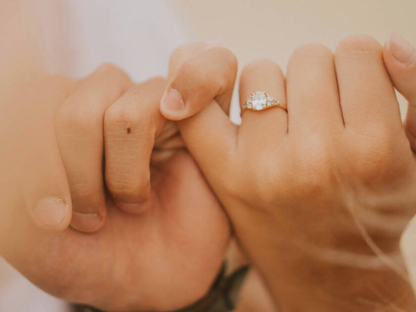 Two hands holding each other by the pinkie fingers. One hand has a diamond ring.