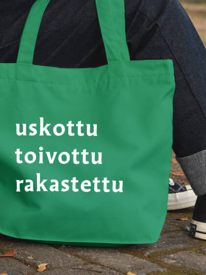 Ihminen istuu portailla, tennarien vieressä näkyy kangaskassi, jossa lukee uskottu toivottu rakastettu.
