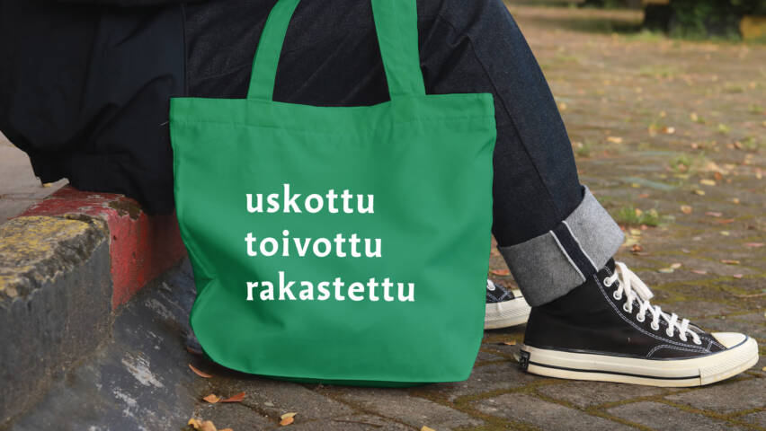 Ihminen istuu portailla, tennarien vieressä näkyy kangaskassi, jossa lukee uskottu toivottu rakastettu.
