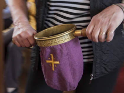 Aikuinen kolehtihaavi kädessään. Kolehtihaavin väri on purppura ja kankaaseen on kirjailtu ristit.
