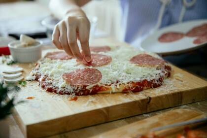 Nuori tekee pizza. Hän asettelee viimeiseksi suolamakkarasiivuja pizzaan.