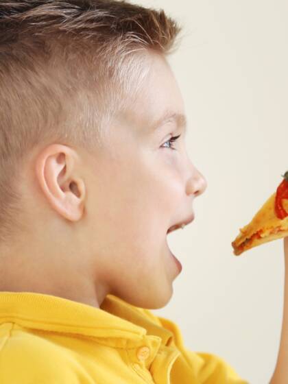 Keltapaitainen lapsi syö pizzaa kädestään.