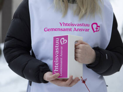Nuori keräyslippaan kanssa, lähikuvassa kädet ja Yhteisvastuukerääjien liivi.