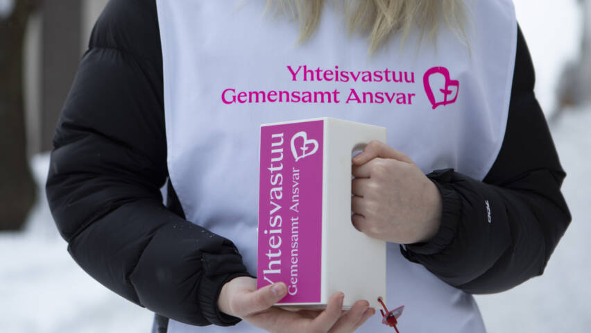 Nuori keräyslippaan kanssa, lähikuvassa kädet ja Yhteisvastuukerääjien liivi.