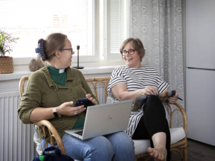 Diakonin kotikäynti. Kaksi henkilöä istuu vierekkäin ikkunan edessä juttelemassa.