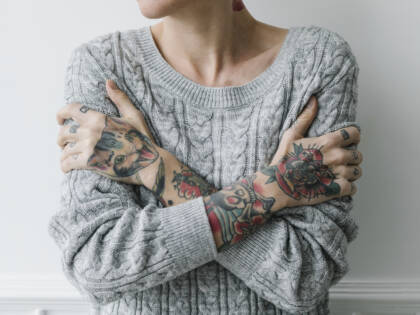 Nuori rajattuna ylävartaloon ja tatuoituihin käsiin, halaa itseään.