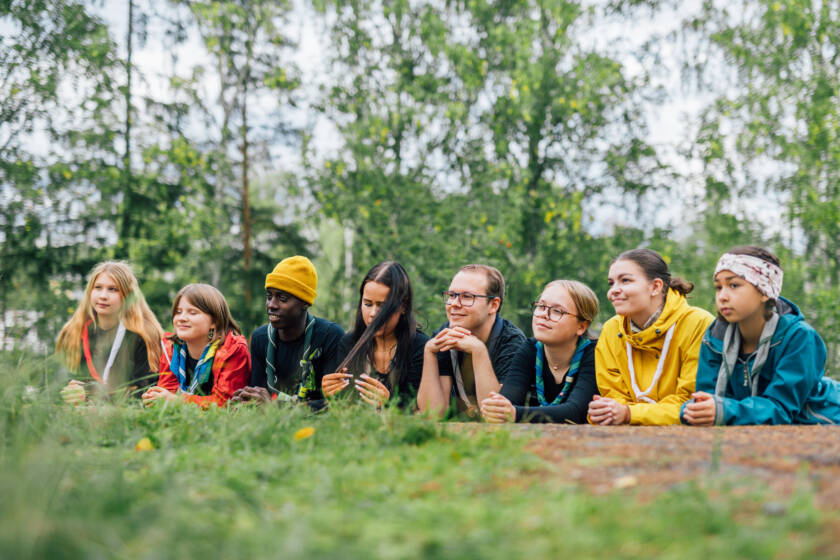 Nuoria partiolaisia luonnossa yhdessä, makaavat rivissä maassa.