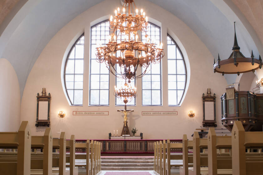 Kirkon sisätila, jossa on suuri ikkuna, kynttilävalaisimia ja alttari. Taustalla näkyy puinen saarnatuoli ja penkit.