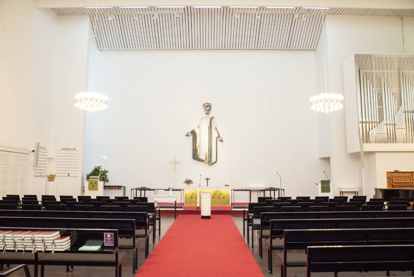 Puijon kirkon kirkkosalin keskikäytävästä näkyy alttaritaulu ja sivuilla kirkon penkkejä.
