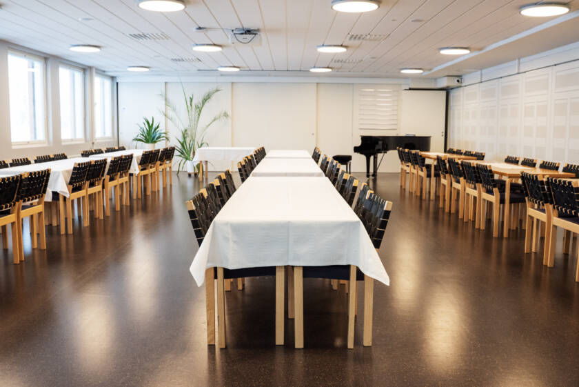 Seurakuntasalissa pitkiä pöytiä.