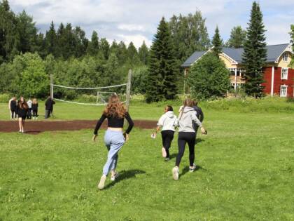 Nuoret pelikentällä. Kesäinen kaunis päivä, taustalla on talo.