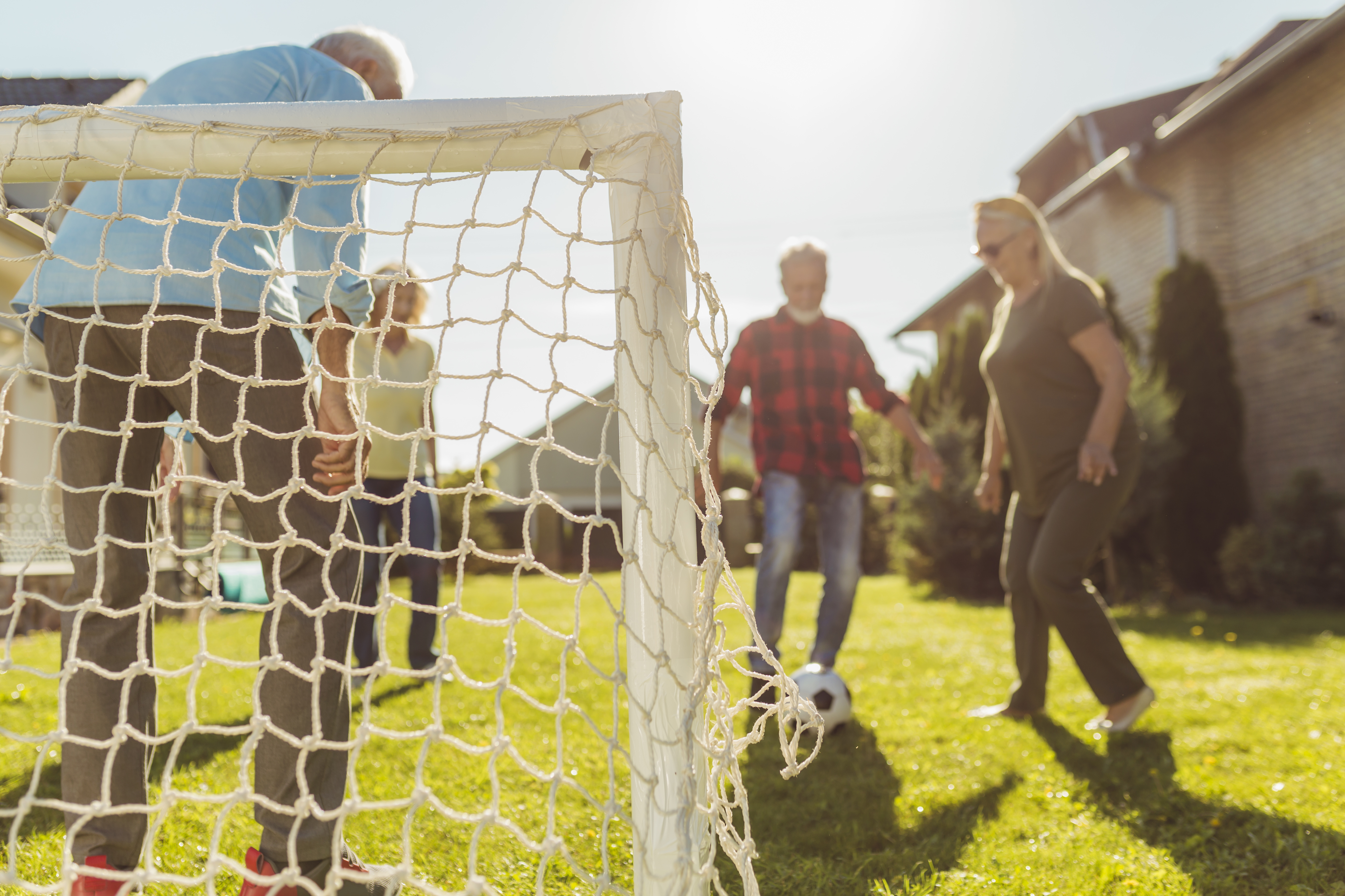 Group of active elderly people having fun playing football on the lawn in the backyard,