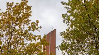 Kirkon torni näkyy puiden välistä, taustalla harmaa taivas. Syksyn lehdet korostavat maiseman värejä.