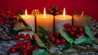 Neljä adventtikynttilää, joista kolmessa liekki puolukka oksa-käpyasetelmassa.