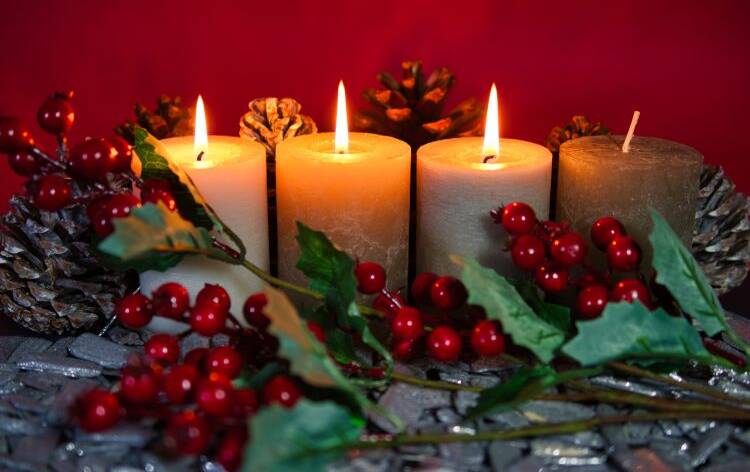 Neljä adventtikynttilää, joista kolmessa liekki puolukka oksa-käpyasetelmassa.