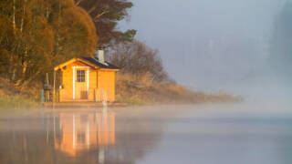 Sauna rakennus rannalla, järvellä usvaa.