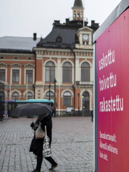 Kuopion kaupungintalon edessä torilla seurakuntavaalien äänestyskontti ja jalankulkija sateenvarjon kanssa.