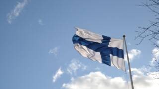 Suomen lippu liehuu tuulessa sinisellä taivaalla.